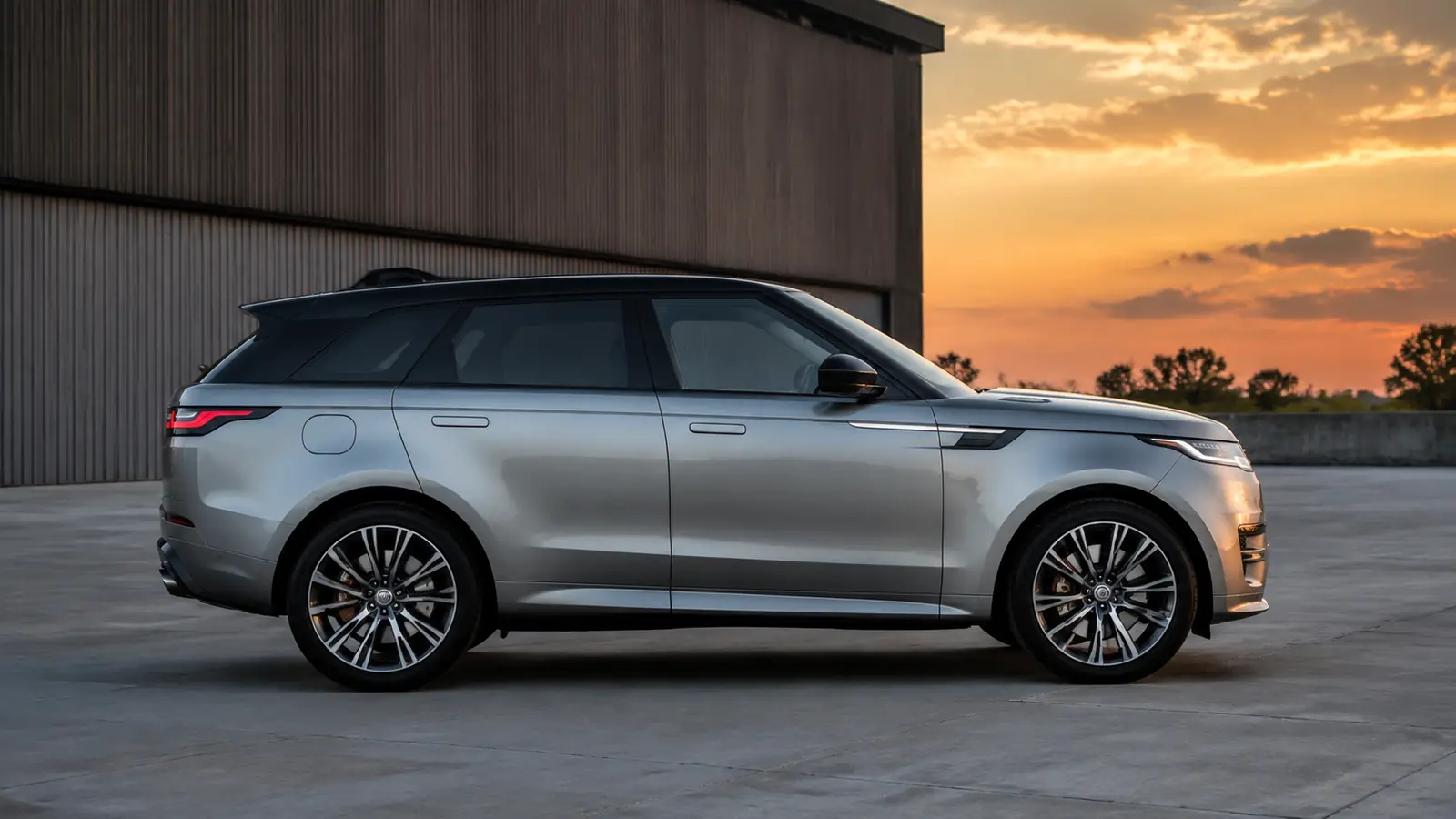 АВТО 1002761 серебристый Range Rover Sport SV крупно в индустриальном дворе на закате
