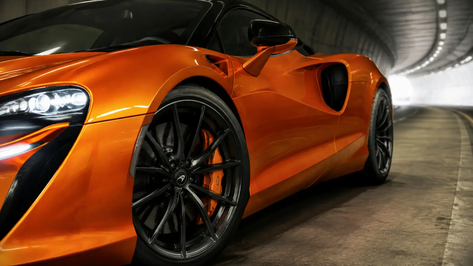 АВТО 1002978 оранжевый McLaren Artura диск и переднее крыло крупным планом в тоннеле с мягким светом
