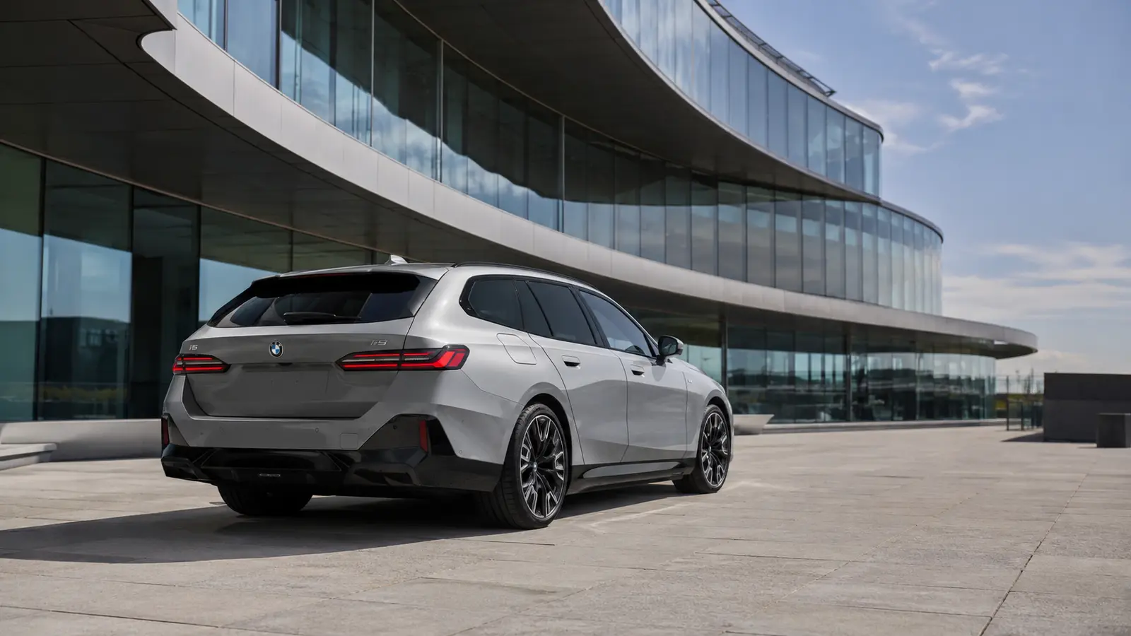 АВТО 1000928 серебристый BMW i5 Touring у стеклянного бизнес-центра