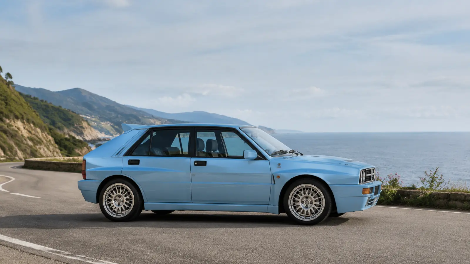 АВТО 1002726 голубой Lancia Delta Integrale крупно на дороге у океана