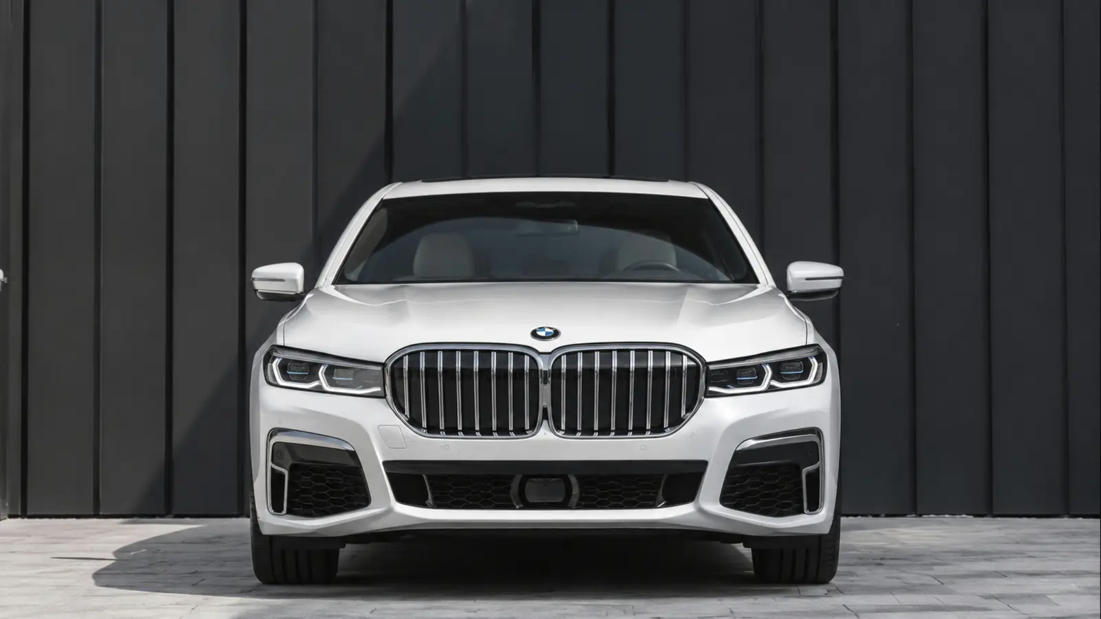 АВТО 1002865 белый BMW 7 серии строго спереди у тёмной современной стены