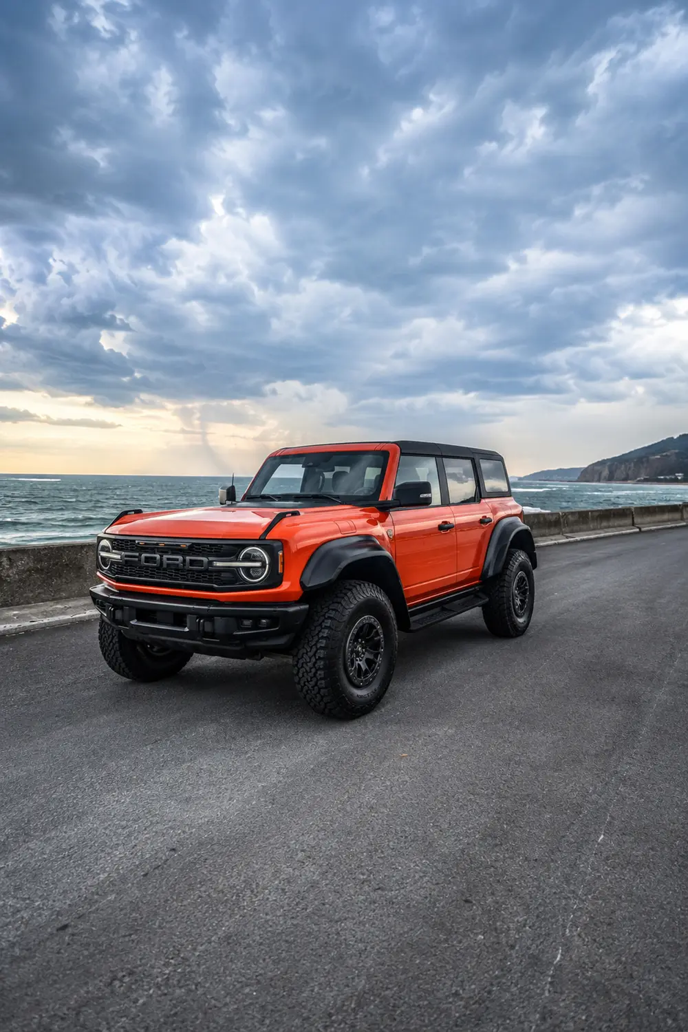 АВТО 1003756 оранжевый Ford Bronco Raptor на прибрежном шоссе
