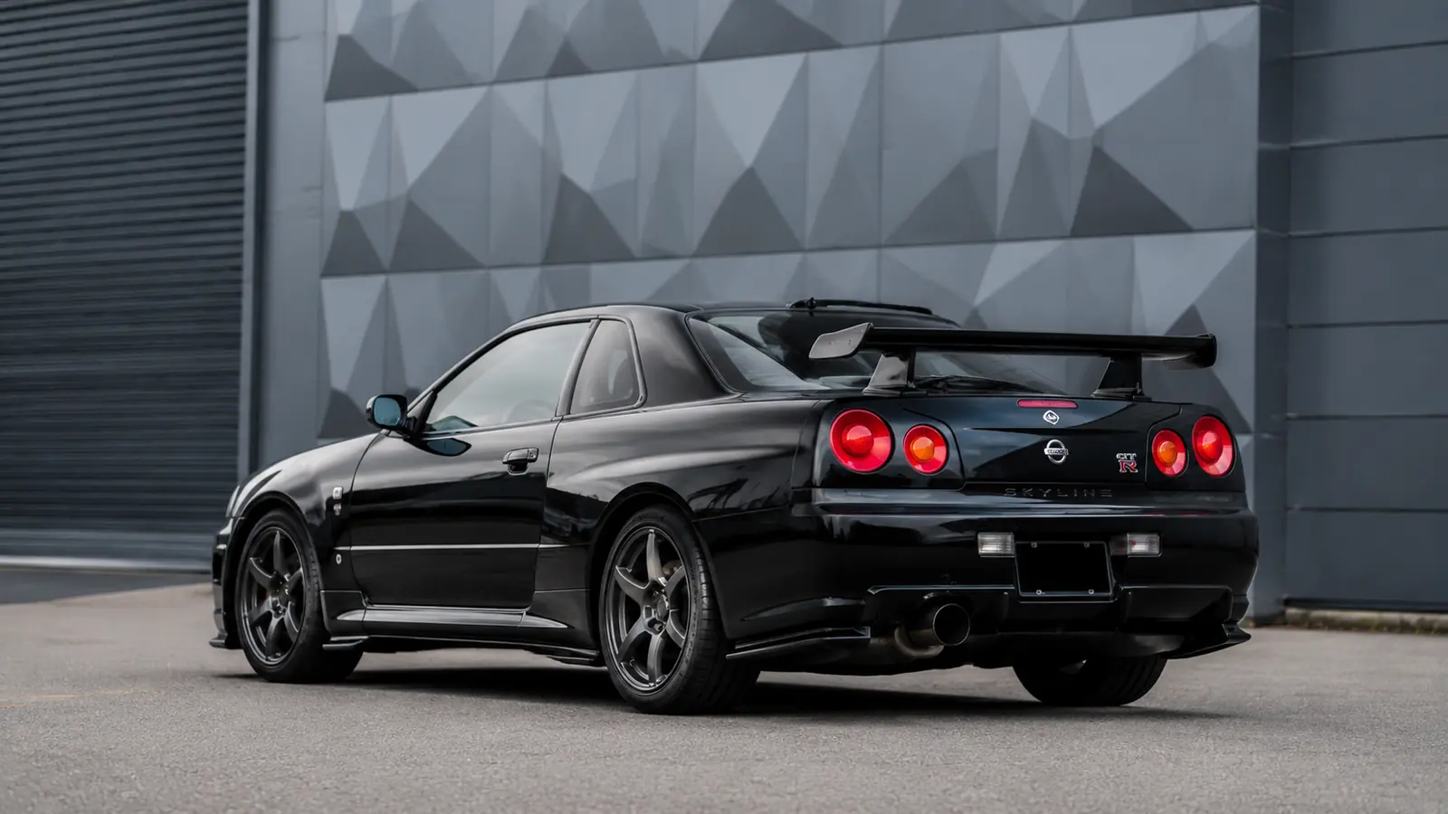 АВТО 1002681 чёрный Nissan Skyline GT-R R34 крупно у геометричного фасада